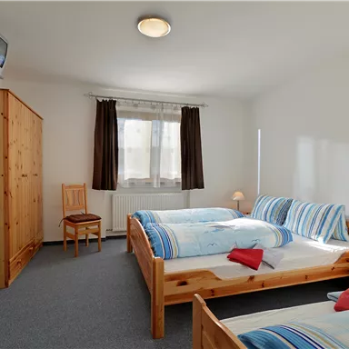 A bright room with two beds and a cozy atmosphere. There is a table, a chair, and a small cupboard.