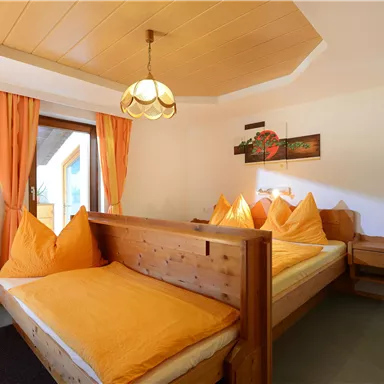 A cozy room with two beds and orange cushions. The atmosphere is bright and inviting, with a window that lets in natural light.