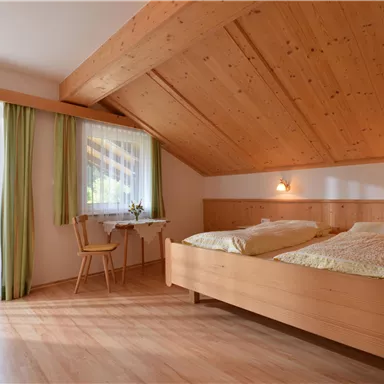 Ein gemütliches Schlafzimmer mit Holzwänden und zwei Einzelbetten. Große Fenster mit Vorhängen lassen viel Licht herein.