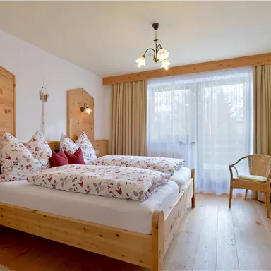 Ein gemütliches Schlafzimmer mit zwei Betten und holzverkleideten Wänden. Große Fenster ermöglichen viel Tageslicht und bieten eine einladende Atmosphäre.