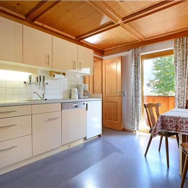 A bright kitchen with modern furniture and a wooden ceiling. A small dining table is next to a window with a view outside.