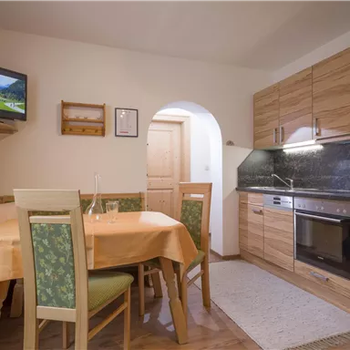 A cozy kitchenette with wooden cabinets and modern appliances. A round table with chairs and a small dining area create an inviting atmosphere.