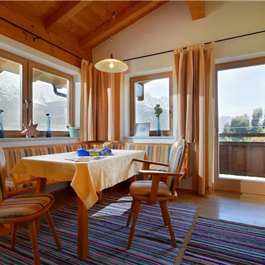 Ein gemütlicher Essbereich mit einem Holztisch und Stühlen. Große Fenster bieten einen Blick auf die Berge und viel Tageslicht.