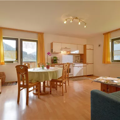 A bright and cozy living kitchen with a dining table and chairs. Large windows offer a view of nature.