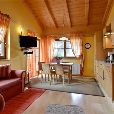 A cozy kitchen with a dining area and a red sofa. The walls are painted yellow and large windows provide plenty of daylight.