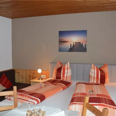 A cozy bedroom with two beds and a stylish headboard. The room decor is modern and inviting, with warm colors and a picture on the wall.