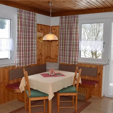 A cozy dining area with wood paneling and large windows. The table is set, and there are comfortable seating options.