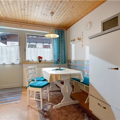 Eine gemütliche Küche mit einem Tisch und Stühlen. Das Zimmer hat helle Wände, einen Holzdecken und große Fenster.