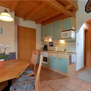 A cozy kitchen with wooden ceilings and modern appliances. The dining area has a table and a small plant.