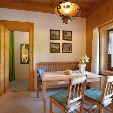 A cozy dining area with wood decor and a table for four people. Pictures hang on the walls, and a window lets in plenty of light.
