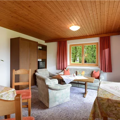 A cozy living area with a dining space and a sofa. Large windows let in plenty of light and offer a view of the greenery.