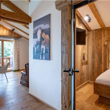 A cozy living environment with wooden beams and a double bed. The room has large windows that let in plenty of light.