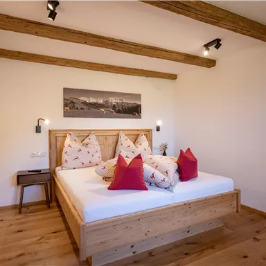 A cozy bedroom with a large double bed and cuddly pillows. The wooden ceiling and the warm floor give it an inviting character.