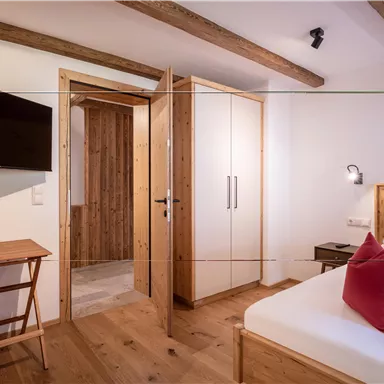 A modern bedroom with a bed, a small table, and a television. The walls are light, and there are wooden details that create a cozy atmosphere.