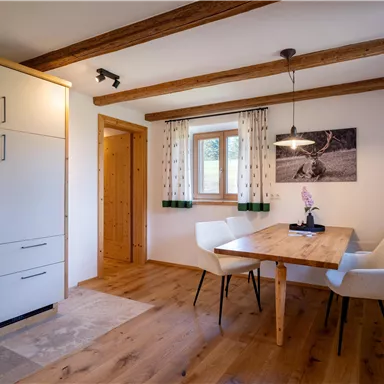 A modern kitchen with wooden shelves and a dining table. Large windows provide plenty of daylight and a cozy atmosphere.