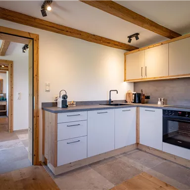 A modern kitchen with wooden details and white furniture. The work surface is space-saving and well-equipped.