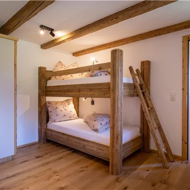 A cozy children's room with a colorful wooden bed and a matching dresser. The room has wooden beams and a warm wooden floor.
