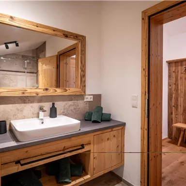 A modern bathroom with a large wooden mirror and an elegant sink. The walls are partially clad in wood, creating a cozy atmosphere.