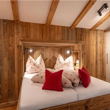 A cozy bedroom with wood paneling and a double bed. The beds are decorated with white and red pillows.