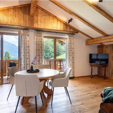 A cozy living space with wooden floors and large windows. The room is bright and offers a view of the surrounding mountains.