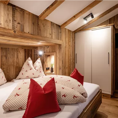 A cozy bedroom with wooden paneling and decorative cushions. The room has a warm atmosphere and modern amenities.