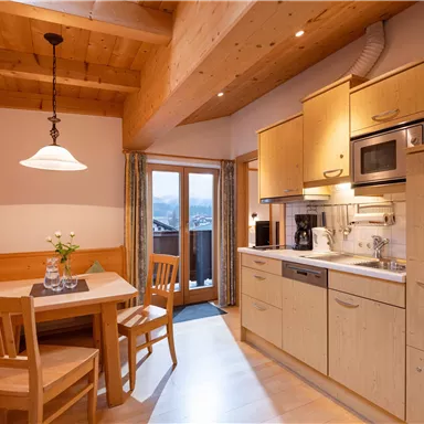 Eine gemütliche Küche mit Holzinterieur, einem Esstisch und Stühlen. Große Fenster sorgen für viel Tageslicht und bieten einen Blick nach draußen.
