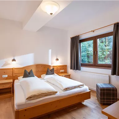 Ein gemütliches Schlafzimmer mit einem Doppelbett und Holzdetails. Ein Fenster mit Blick ins Grüne sorgt für natürliches Licht.
