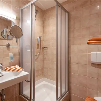 Ein kleines Badezimmer mit Dusche und Waschbecken. Die Wände sind mit braunen Fliesen gefliest, und es gibt orangefarbene Handtücher.