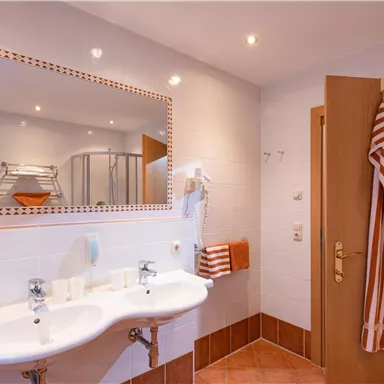 Ein modernes Badezimmer mit zwei Waschbecken und einem großen Spiegel. An der Wand hängen orangefarbene Handtücher und ein Bademantel.