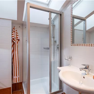 Ein modernes Badezimmer mit einer Duschkabine und einem Waschbecken. Orange und weiße Handtücher sind auf dem Waschbecken platziert.