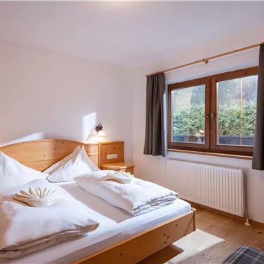 Ein gemütliches Schlafzimmer mit einem Doppelbett und Holzmöbeln. Das Zimmer hat ein Fenster mit Blick ins Grüne und einen Fernseher.