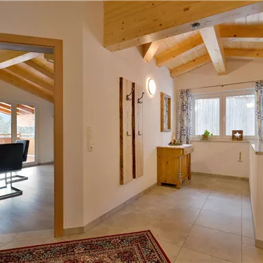 Ein einladender Flur mit einer Holzwand und einem Teppich. Im Hintergrund ist ein offenes Büro mit einem Schreibtisch und einem Fenster, das Licht hereinlässt.