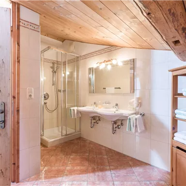 Ein modernes Badezimmer mit einer Dusche und zwei Waschbecken. Es ist hell und freundlich, mit Holz- und Flieselementen.