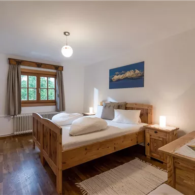 Ein gemütliches Schlafzimmer mit Holzmöbeln und einem großen Fenster. Es gibt zwei Betten sowie einen kleinen Tisch mit einer Zeitschrift.