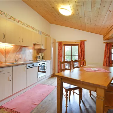 Eine moderne Küche mit Holzdecke und warmen Farben. Der Esstisch ist aus Holz und lädt zum gemütlichen Beisammensein ein.
