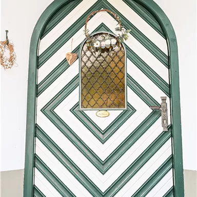A striking door with a diagonal green and white pattern. Above the door hangs a decorative fabric with small details.