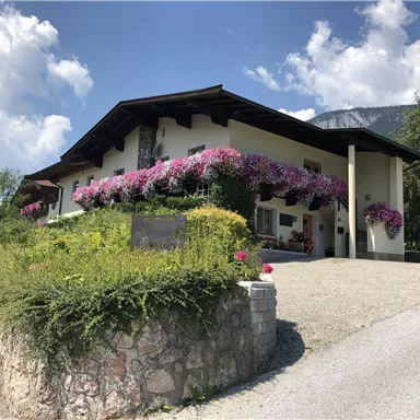 Ein schönes Haus mit bunten Blumen und viel Grün. Der Himmel ist klar und die Umgebung ist ruhig und einladend.