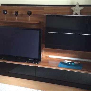 A modern living room with a black television on an elegant TV stand. On top, glasses and a decorative star figure are visible.