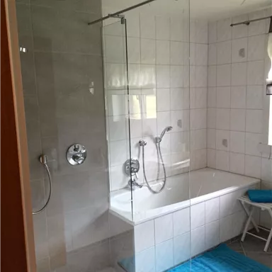 A modern bathroom with a shower and a bathtub. White tiles and a blue bath mat give the room a fresh look.