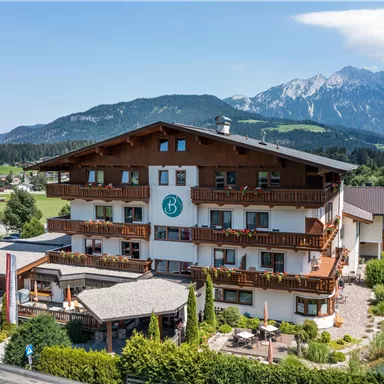 Ein charmantes Hotel im alpinen Stil mit mehreren Balkonen. Im Hintergrund sind majestätische Berge und eine grüne Landschaft zu sehen.