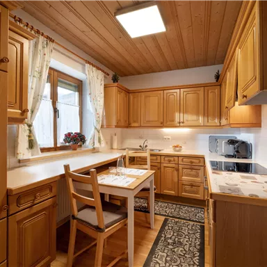 A cozy kitchen with wooden cabinets and a dining table. The large windows provide bright light and a pleasant atmosphere.