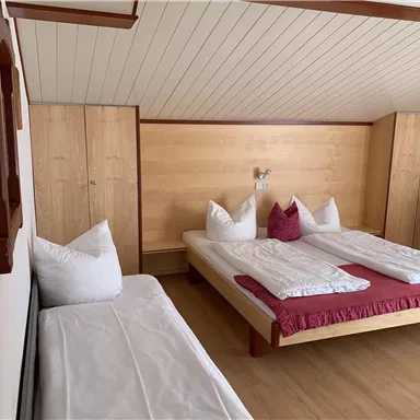 A cozy room with two beds and an additional bed. The walls are bright, and the furnishings are made of wood, creating a warm atmosphere.