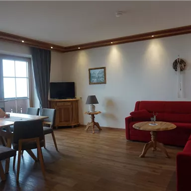 A cozy living room with a red couch and a wooden table. Large windows let in plenty of light and create an inviting atmosphere.