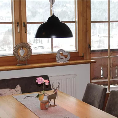 A cozy dining area with a wooden table and modern chairs. Large windows offer a view of a snowy landscape.