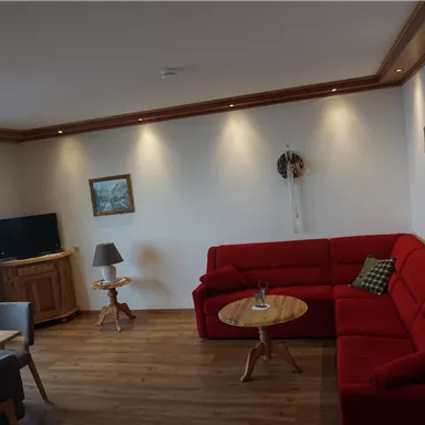 A cozy living room with a red sofa and a wooden table. There is a television and some pictures on the wall.