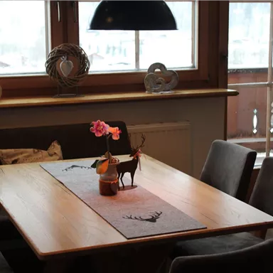 A cozy dining area with a wooden table and modern chairs. On the table, there is a flower in a vase and a small figurine of a deer.