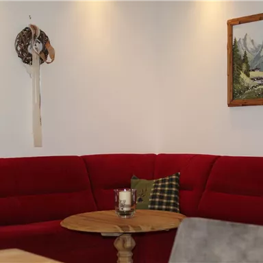 A cozy living room with a red sofa and a wooden table. There is a painting of mountains and a river hanging on the wall.