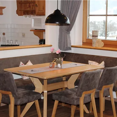 A cozy dining area with a wooden table and upholstered chairs. Large windows provide plenty of light and a view of the winter landscape.