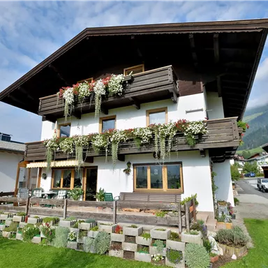Ein charmantes Haus mit Blumenkästen und einem großen Garten. Im Hintergrund sind sanfte Hügel und ein klarer Himmel sichtbar.