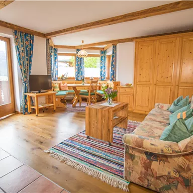 A cozy living room with wooden floors and rustic furniture. Large windows provide plenty of daylight and a view of nature.